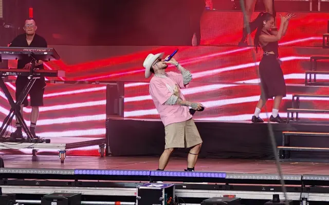 Artista de Latin Fest canta con sombrero blanco ante un escenario iluminado en rojo