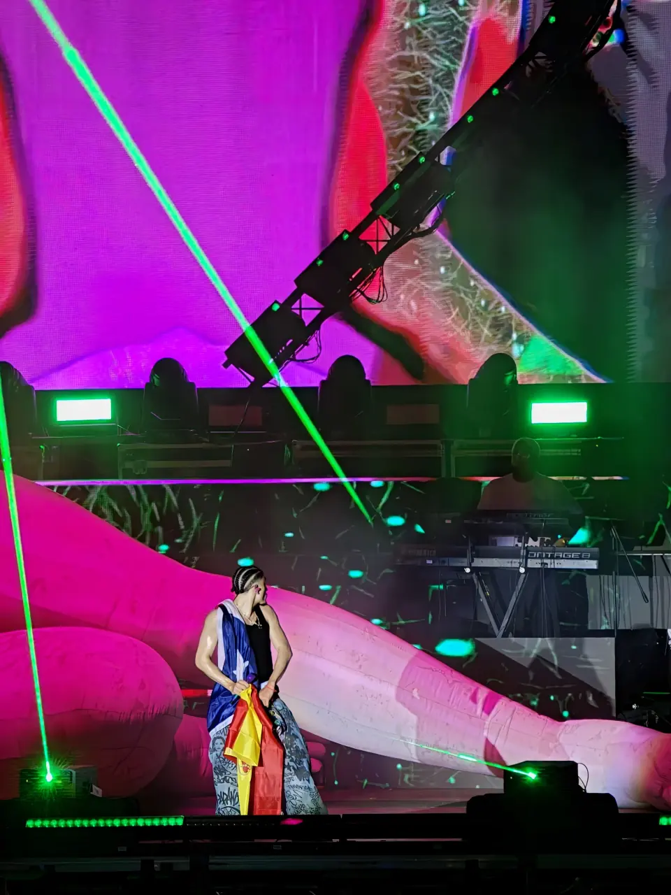 Artista de Latin Fest sostiene una bandera de España entre luces verdes y visuales rosas